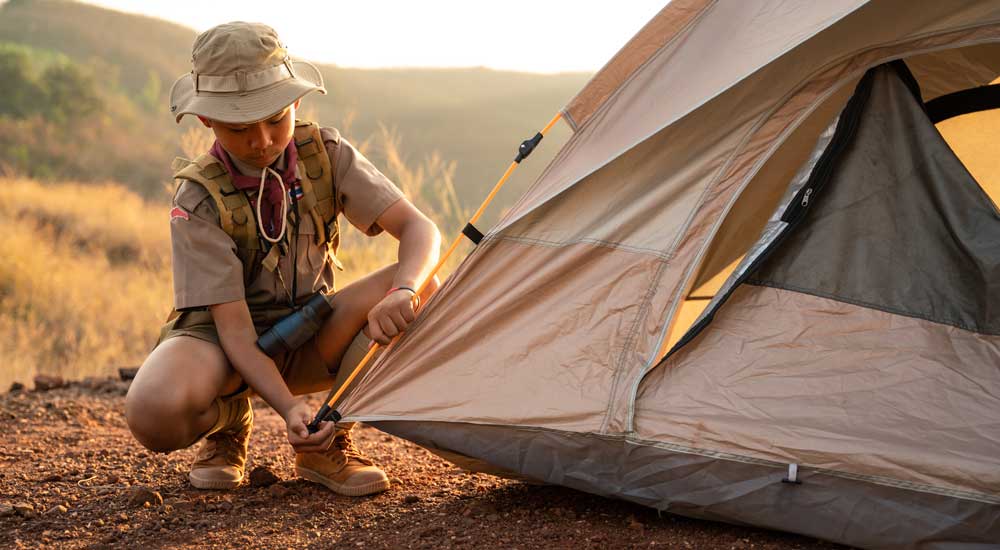 young boy in uniform adjusting tent outdoors