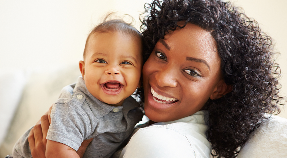 A woman joyfully cradling her baby, both wearing contented smiles, radiating love and happiness.