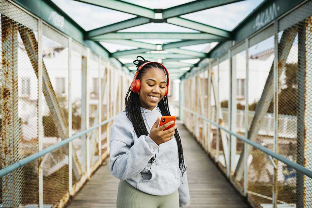 young woman outside looking at phone with earphones on