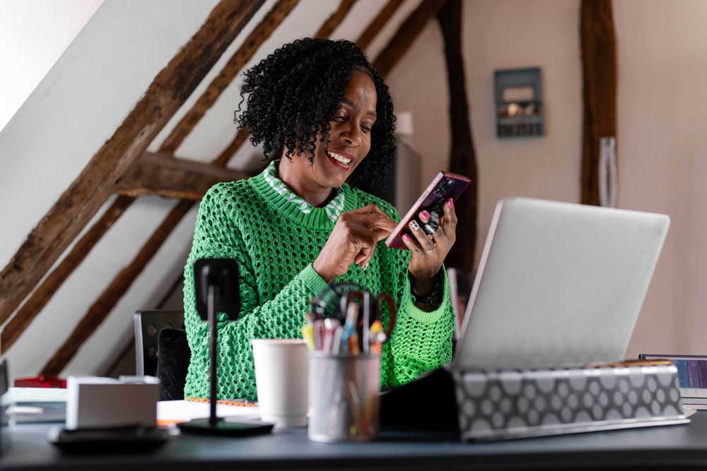 woman sitting at table with laptop and cell phone