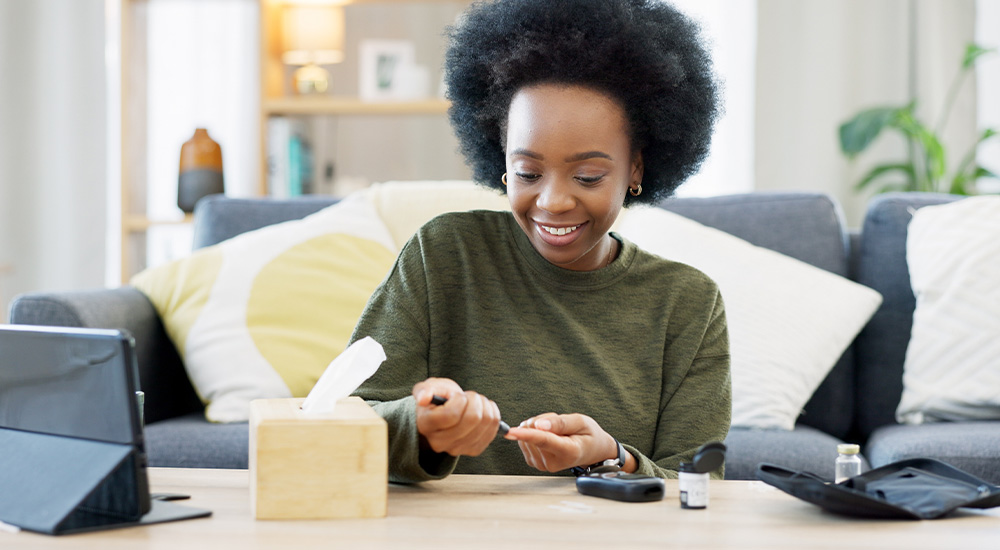 woman pricking finger at table with glucose monitor